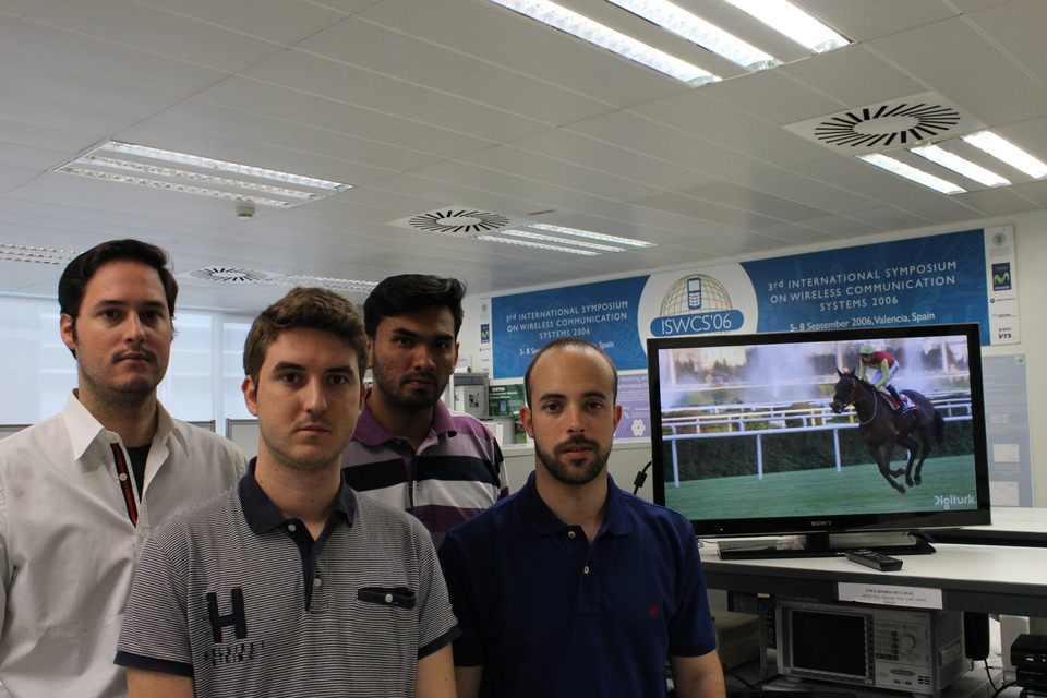 Four people in a lab in front of a TV demo